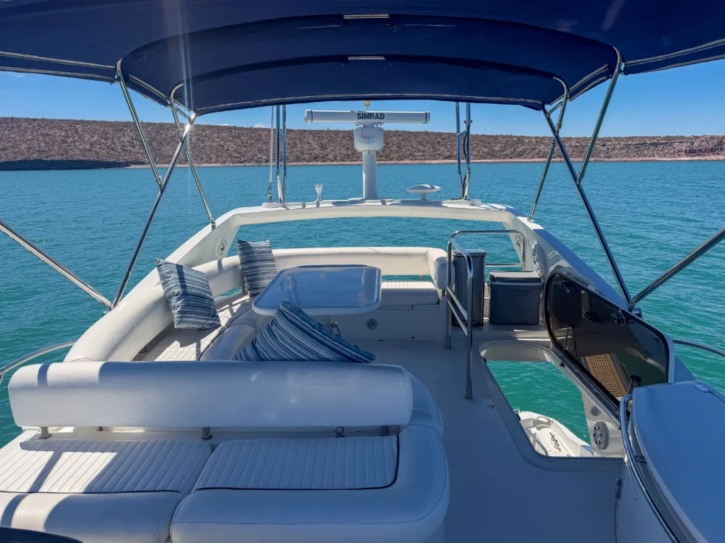 Seating area on a white boat with blue striped cushions under a blue canopy, turquoise water ahead and a Simrad radar mounted at the helm.