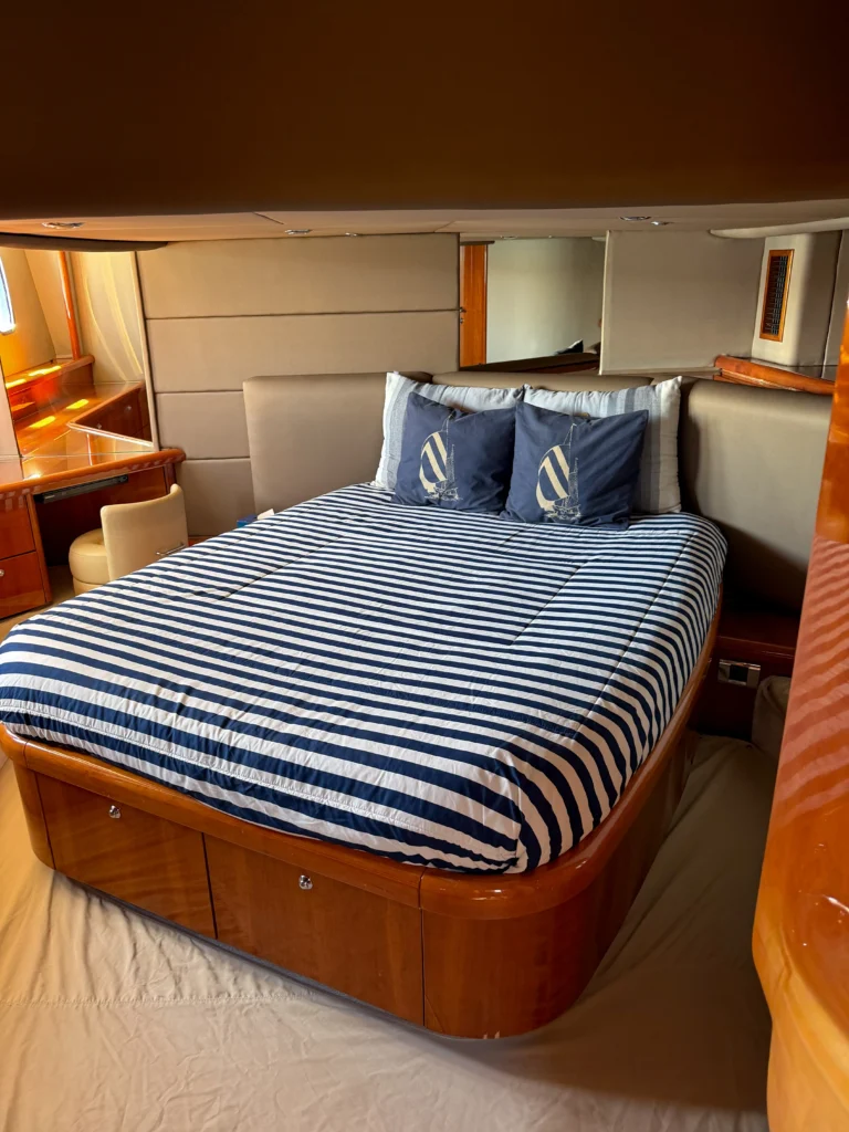 Boutique yacht cabin with a large striped navy-and-white bed, beige padded headboard, and wooden storage cabinets.