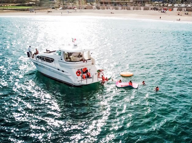 Cabo2Vegas anchored near the beach while guests swim and float beside the yacht
